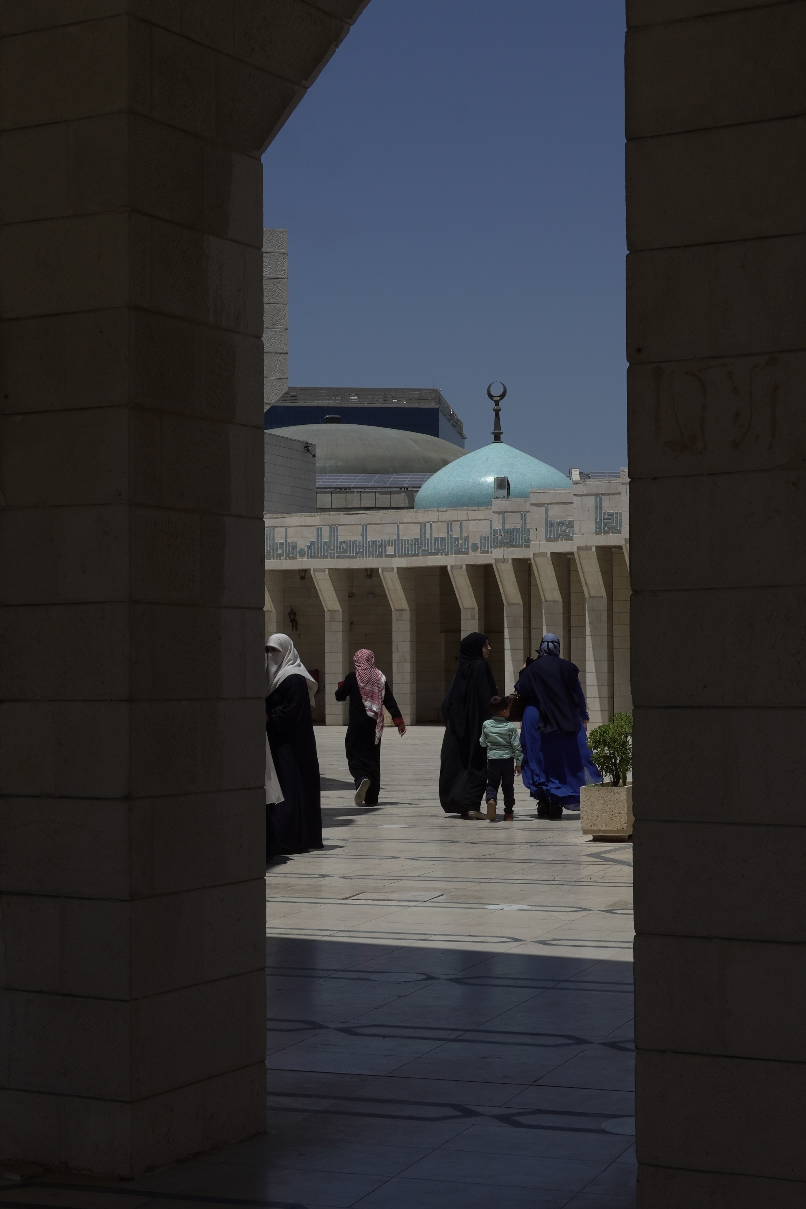 People walking through Islamic architectural complex with turquoise dome