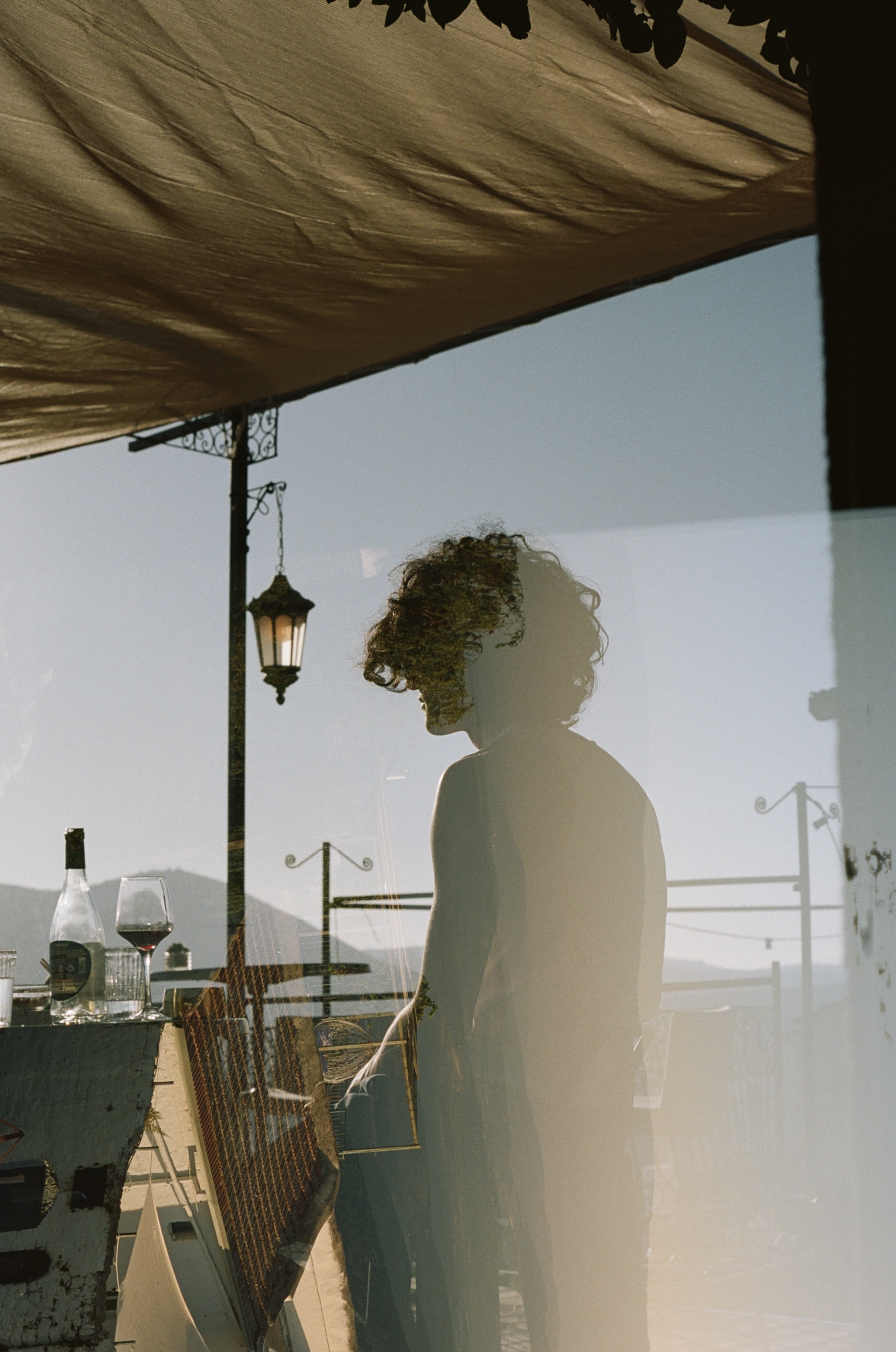 Person silhouetted on boat deck with lantern and wine, enjoying golden hour views